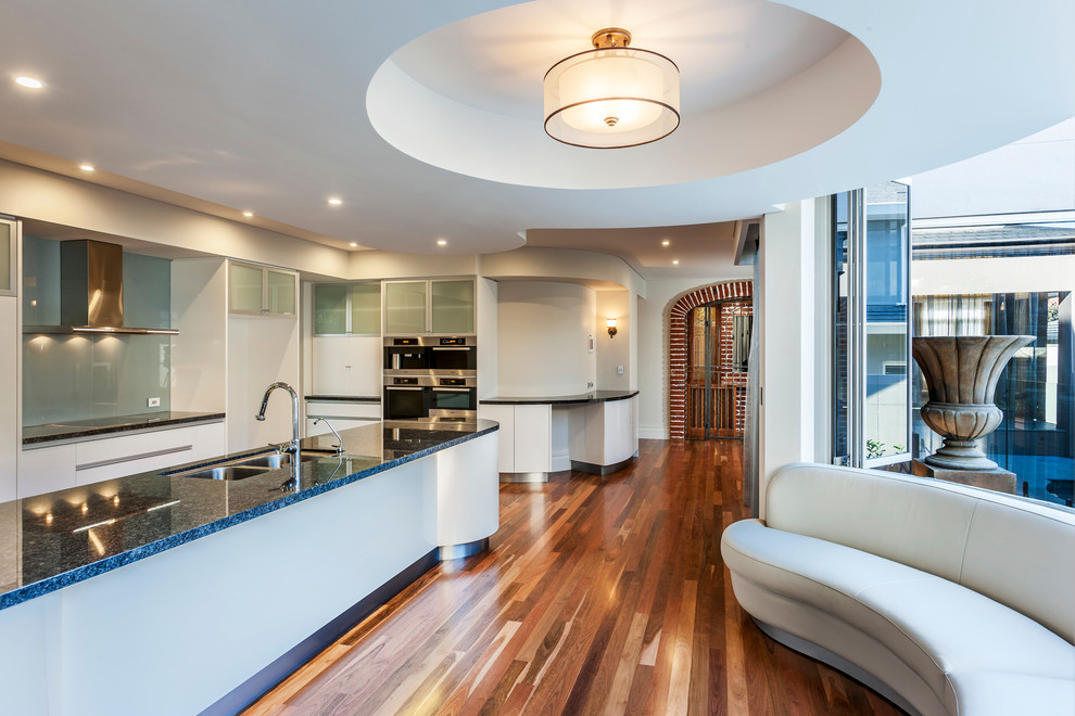 Large contemporary galley open plan kitchen in Perth with a submerged sink, flat-panel cabinets, white cabinets, engineered stone countertops, blue splashback, glass sheet splashback, stainless steel appliances, medium hardwood flooring and an island.