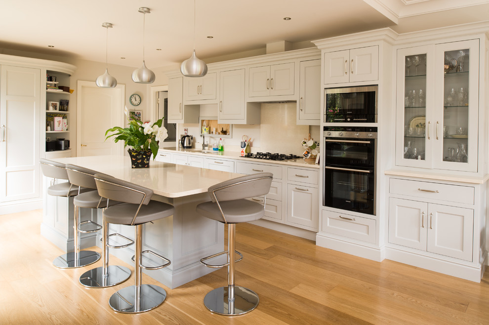Elegant single-wall medium tone wood floor kitchen photo in Dublin with recessed-panel cabinets, white cabinets, black appliances and an island
