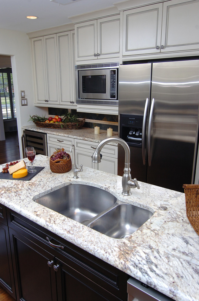 Example of a classic u-shaped eat-in kitchen design in Dallas with an undermount sink, recessed-panel cabinets, white cabinets, granite countertops, gray backsplash, stone tile backsplash and stainless steel appliances