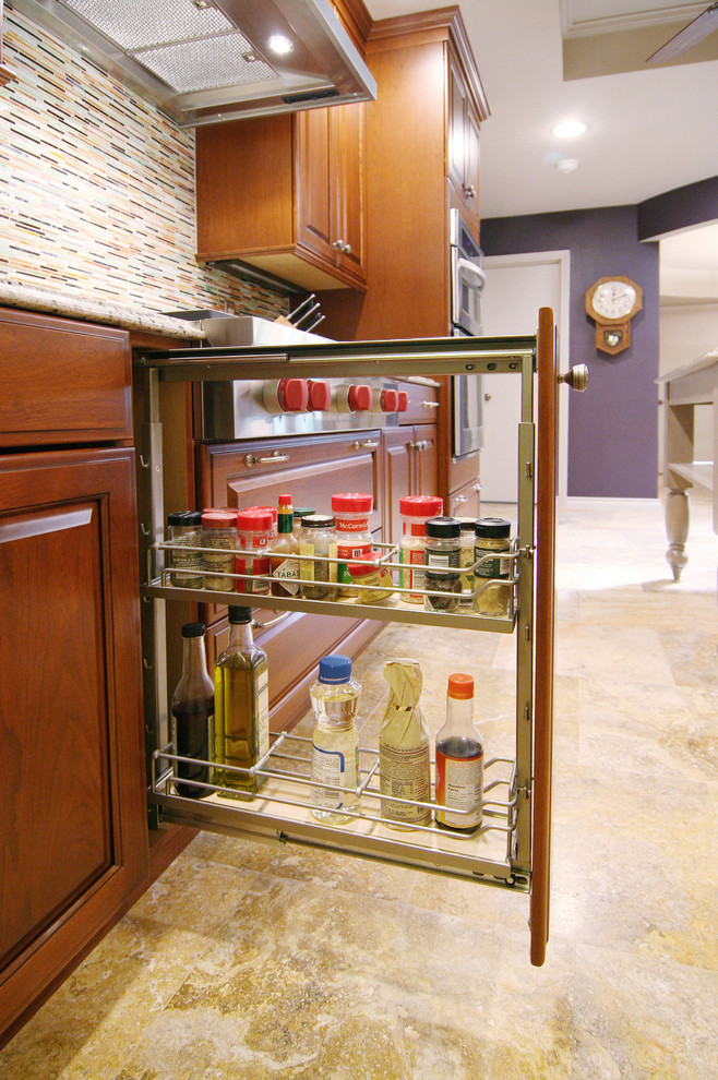 Klassisk inredning av ett kök, med en undermonterad diskho, luckor med upphöjd panel, skåp i mellenmörkt trä, granitbänkskiva, flerfärgad stänkskydd och rostfria vitvaror