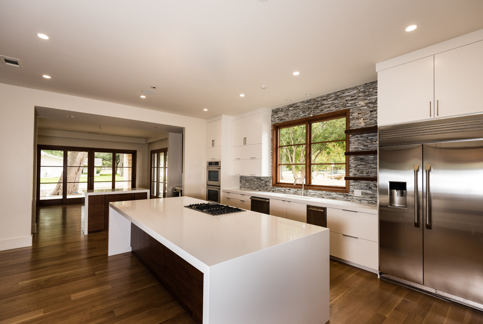 Inredning av ett modernt stort kök, med vita skåp, laminatbänkskiva, grått stänkskydd, en köksö, en enkel diskho, släta luckor, stänkskydd i stickkakel, rostfria vitvaror, mellanmörkt trägolv och brunt golv