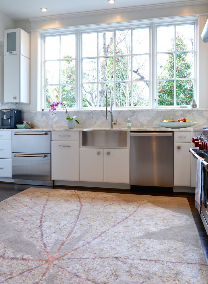 Modern inredning av ett kök, med rostfria vitvaror, släta luckor, vita skåp, vitt stänkskydd och stänkskydd i sten