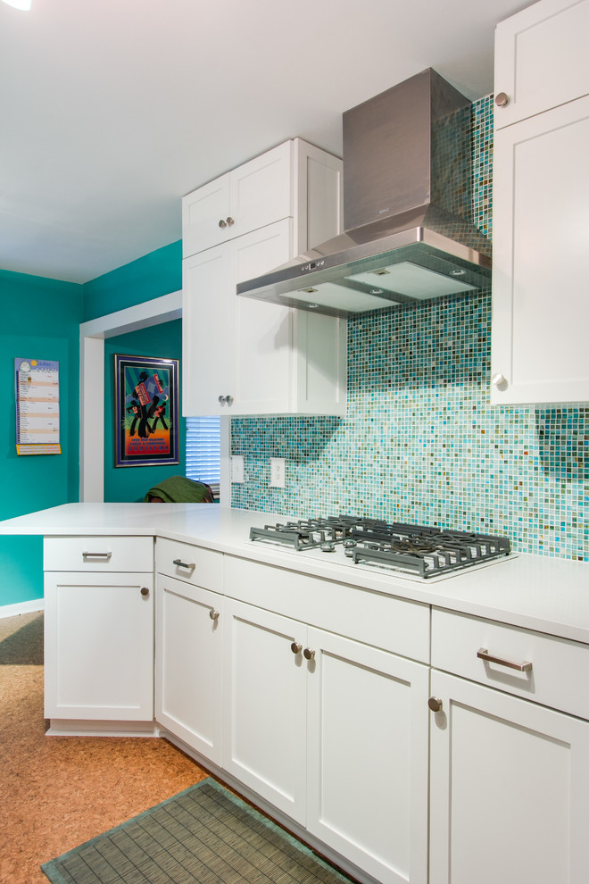 This is an example of a small eclectic galley enclosed kitchen in Dallas with a submerged sink, shaker cabinets, white cabinets, engineered stone countertops, multi-coloured splashback, glass sheet splashback, white appliances, cork flooring, a breakfast bar, brown floors and white worktops.