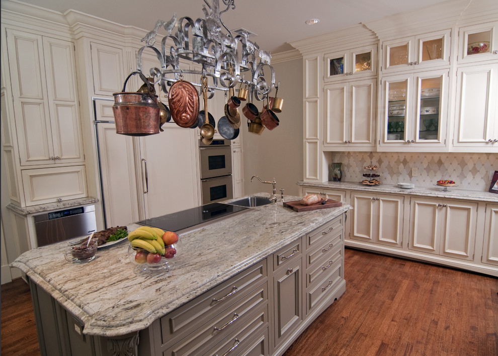 Klassisk inredning av ett kök, med en rustik diskho, luckor med infälld panel, gröna skåp, granitbänkskiva, beige stänkskydd, stänkskydd i stenkakel och integrerade vitvaror