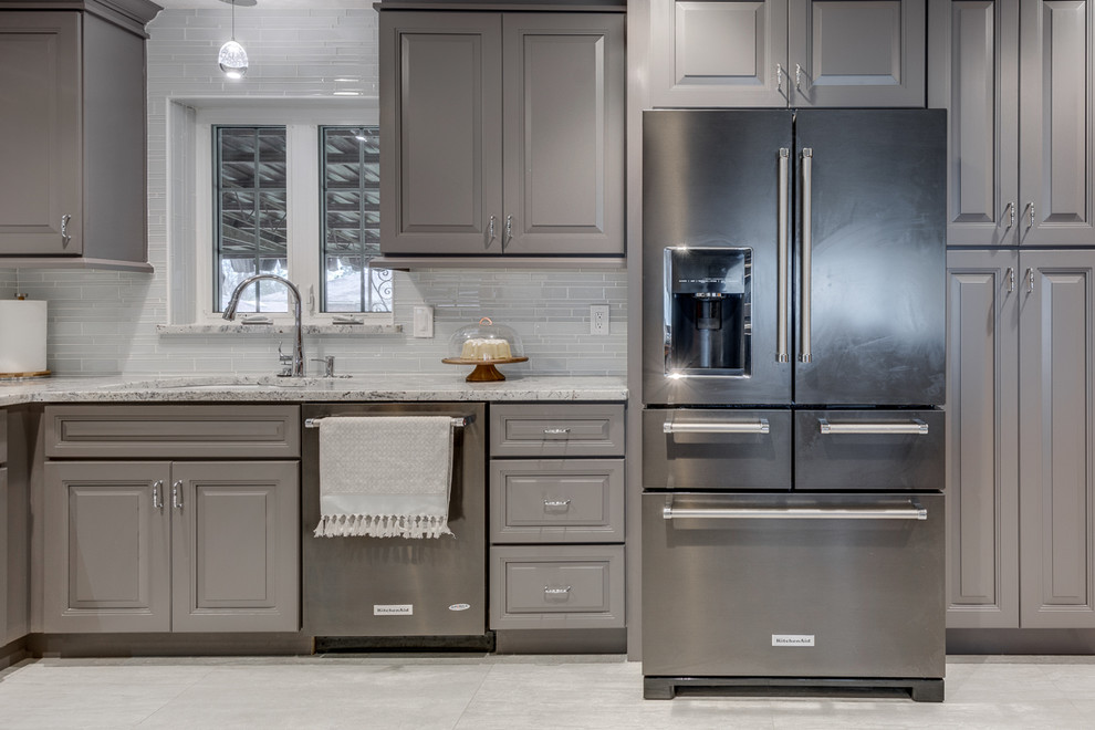 Example of a minimalist l-shaped porcelain tile kitchen pantry design in Dallas with a drop-in sink, gray cabinets, granite countertops, gray backsplash, glass tile backsplash, black appliances, raised-panel cabinets and no island