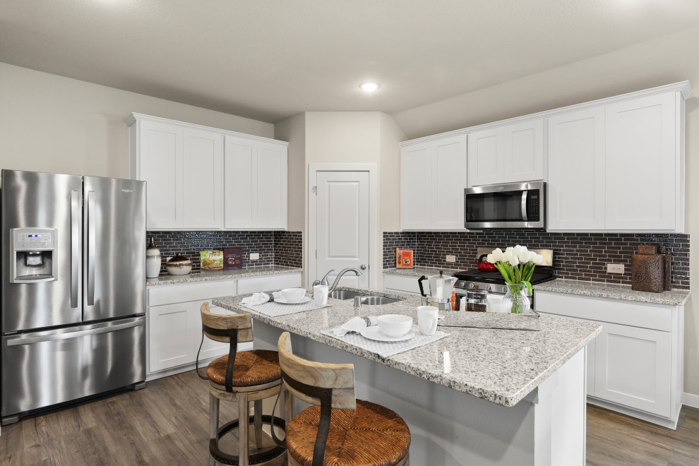 This is an example of a medium sized contemporary l-shaped kitchen/diner in Dallas with recessed-panel cabinets, white cabinets, granite worktops, black splashback, metro tiled splashback, stainless steel appliances, medium hardwood flooring, an island, brown floors and multicoloured worktops.