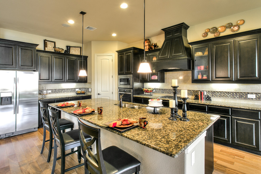 Eat-in kitchen - large traditional l-shaped light wood floor eat-in kitchen idea in Dallas with an undermount sink, raised-panel cabinets, black cabinets, granite countertops, multicolored backsplash, glass tile backsplash, stainless steel appliances and an island