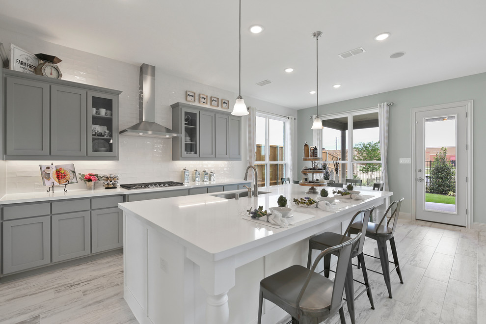 Example of a mid-sized country gray floor eat-in kitchen design in Dallas with an undermount sink, solid surface countertops, white backsplash, subway tile backsplash, an island, white countertops, shaker cabinets and gray cabinets