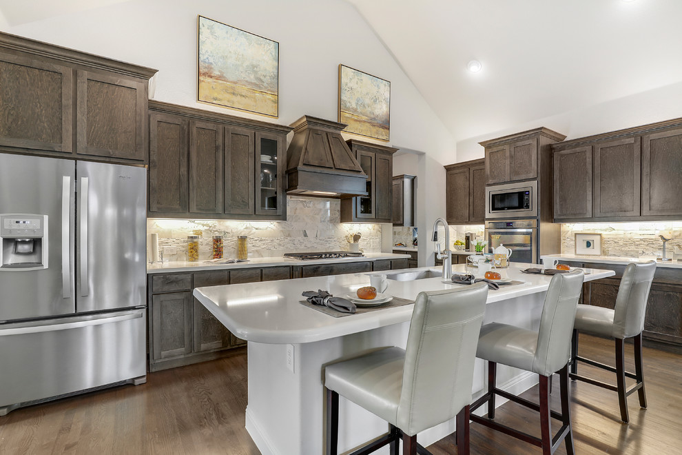 Inspiration for a traditional kitchen in Dallas with dark wood cabinets, composite countertops, stone tiled splashback, stainless steel appliances, an island, brown floors, white worktops, a single-bowl sink, shaker cabinets and dark hardwood flooring.