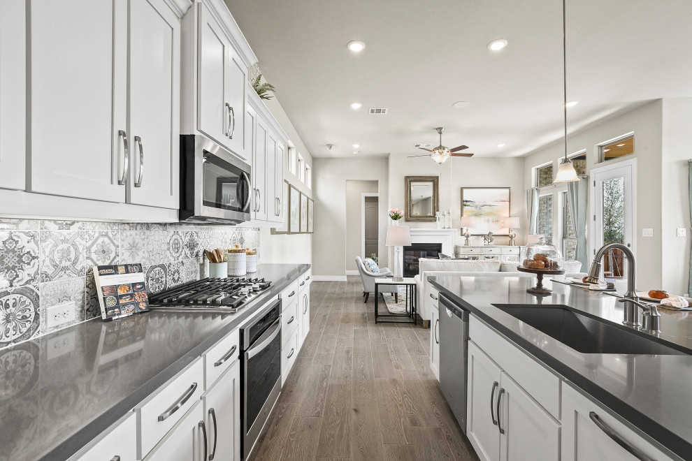 Bild på ett litet funkis grå grått l-kök, med en undermonterad diskho, luckor med infälld panel, vita skåp, bänkskiva i koppar, flerfärgad stänkskydd, stänkskydd i keramik, rostfria vitvaror, ljust trägolv, en köksö och brunt golv