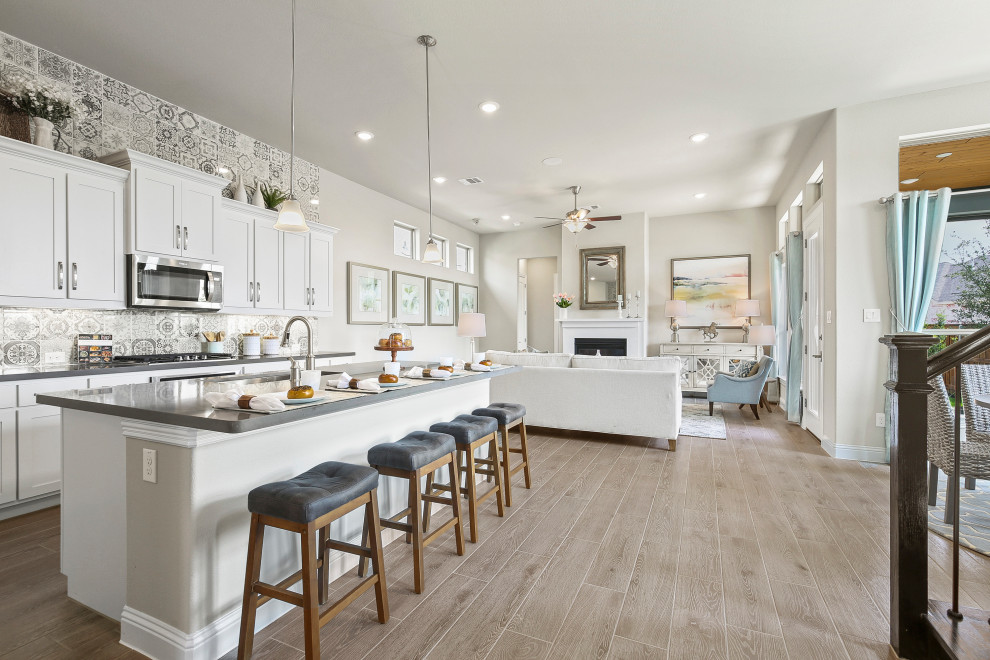 Mid-sized trendy l-shaped medium tone wood floor and brown floor eat-in kitchen photo in Dallas with a triple-bowl sink, recessed-panel cabinets, white cabinets, solid surface countertops, multicolored backsplash, ceramic backsplash, stainless steel appliances, an island and gray countertops