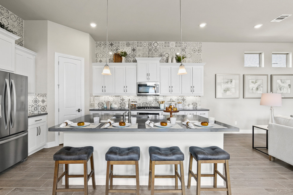 Example of a mid-sized trendy l-shaped medium tone wood floor and brown floor eat-in kitchen design in Dallas with a triple-bowl sink, recessed-panel cabinets, white cabinets, solid surface countertops, multicolored backsplash, ceramic backsplash, stainless steel appliances, an island and gray countertops