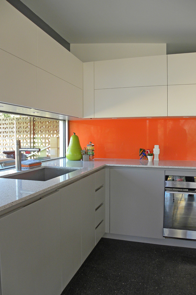 Стильный дизайн: кухня в стиле ретро с оранжевым фартуком, фартуком из стекла, плоскими фасадами, белыми фасадами и окном - последний тренд