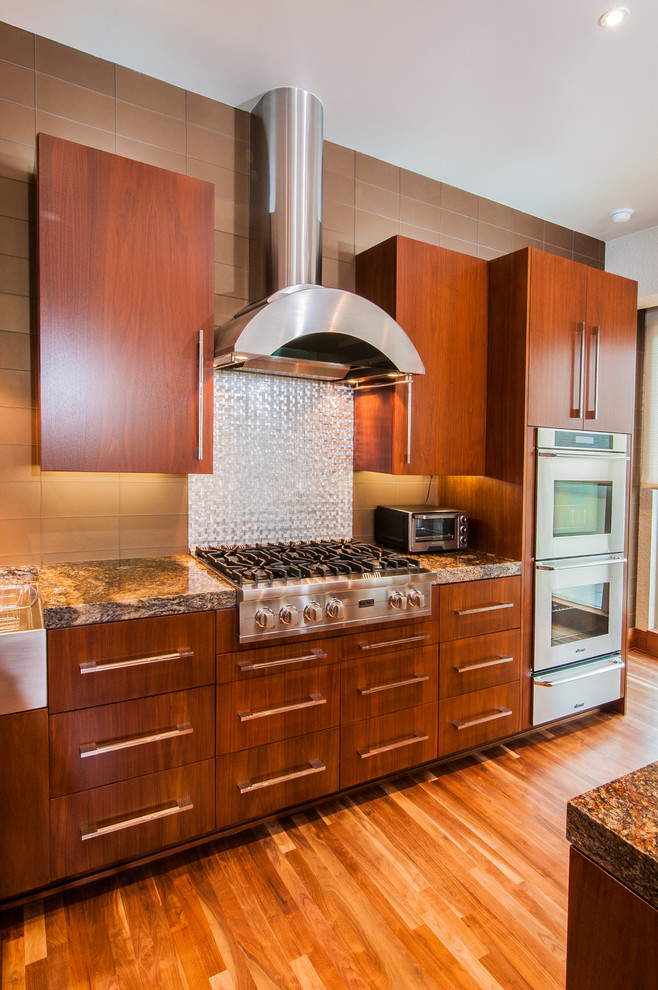 Exemple d'une cuisine américaine parallèle tendance en bois brun avec un évier de ferme, un plan de travail en granite, une crédence métallisée, une crédence en dalle métallique et un électroménager en acier inoxydable.