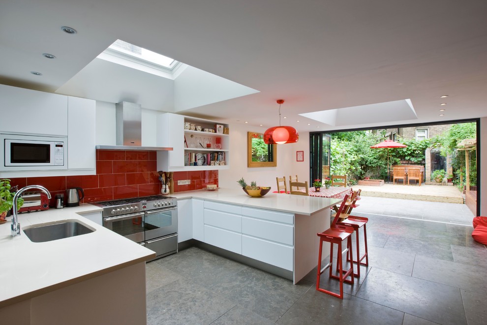 Modern inredning av ett mellanstort kök, med en undermonterad diskho, släta luckor, vita skåp, bänkskiva i kvartsit, rött stänkskydd, stänkskydd i glaskakel, rostfria vitvaror och marmorgolv