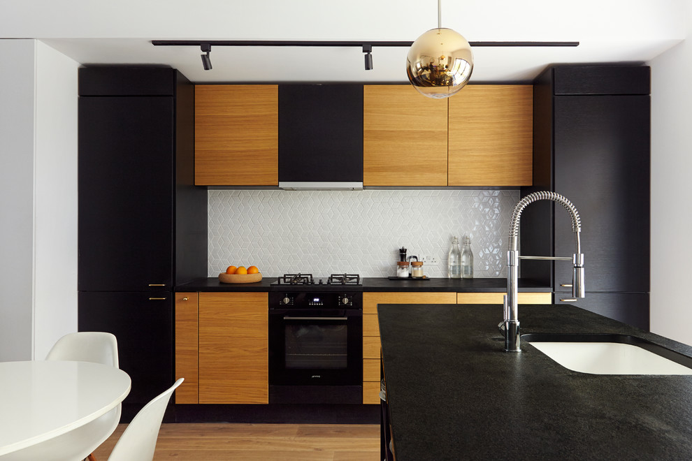 Einzeilige Moderne Wohnküche mit Unterbauwaschbecken, flächenbündigen Schrankfronten, Küchenrückwand in Weiß, schwarzen Elektrogeräten, hellem Holzboden und Kücheninsel in London