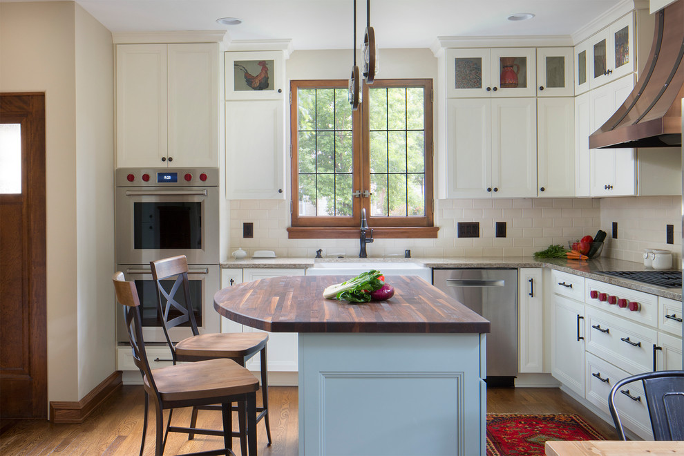 Eat-in kitchen - mid-sized traditional l-shaped medium tone wood floor eat-in kitchen idea in Milwaukee with a farmhouse sink, white cabinets, quartzite countertops, white backsplash, subway tile backsplash, stainless steel appliances, an island, recessed-panel cabinets and gray countertops