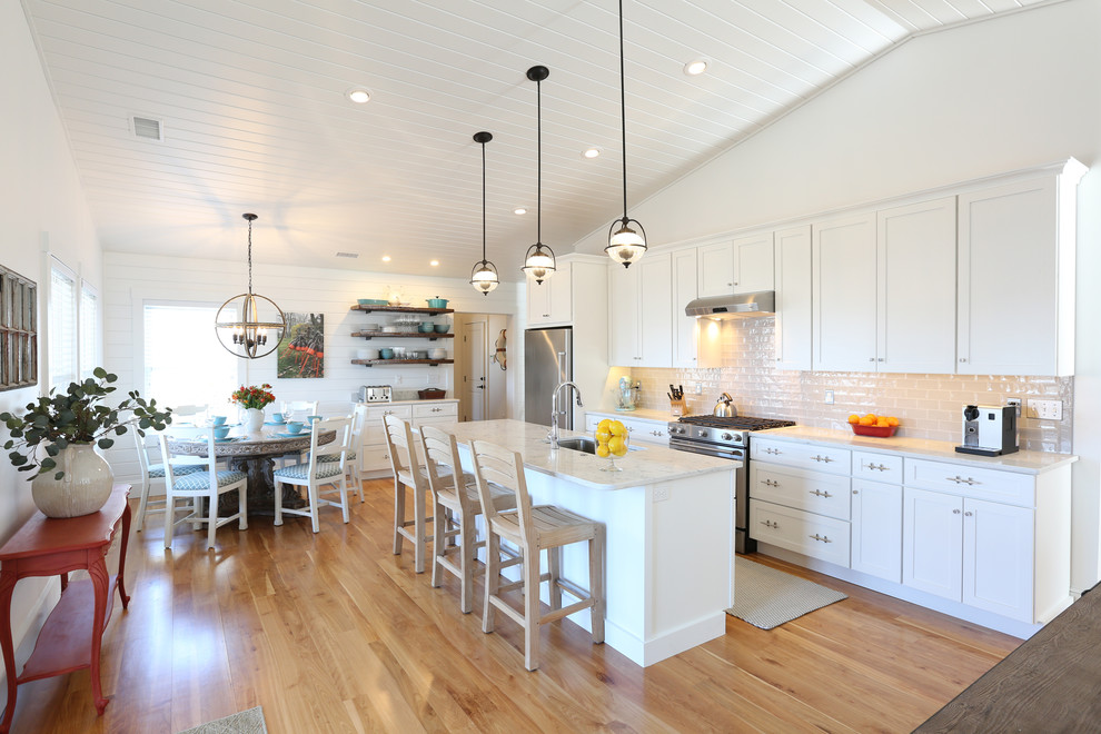 Beach style kitchen/diner in Portland Maine with a submerged sink, white cabinets, engineered stone countertops, white splashback, stainless steel appliances, an island, shaker cabinets, metro tiled splashback, light hardwood flooring and beige floors.