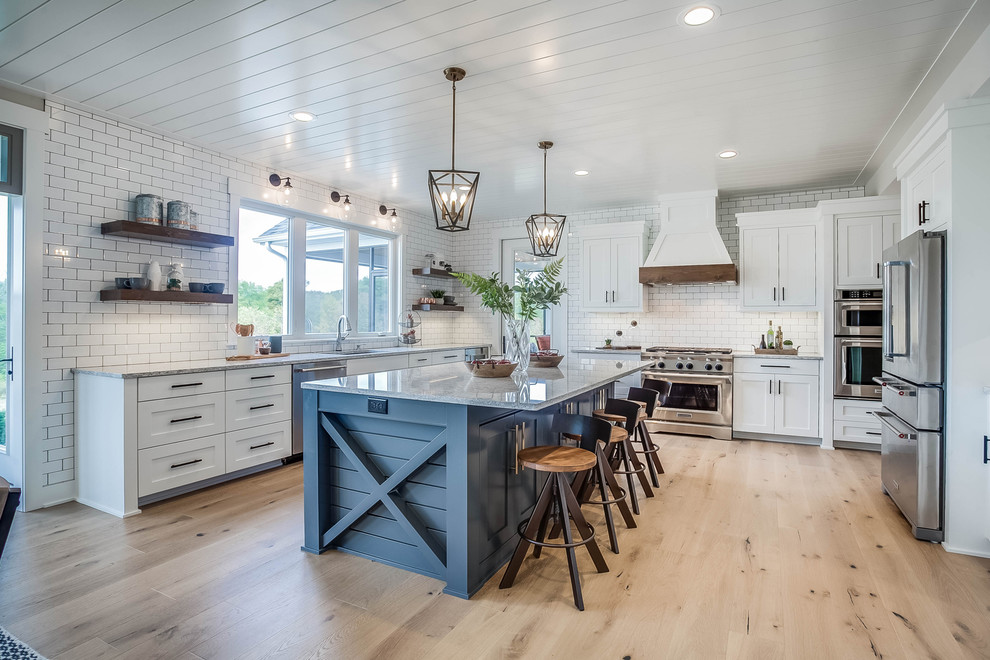 Design ideas for a farmhouse u-shaped open plan kitchen in Grand Rapids with a submerged sink, shaker cabinets, white cabinets, white splashback, metro tiled splashback, stainless steel appliances, light hardwood flooring, an island, beige floors and grey worktops.
