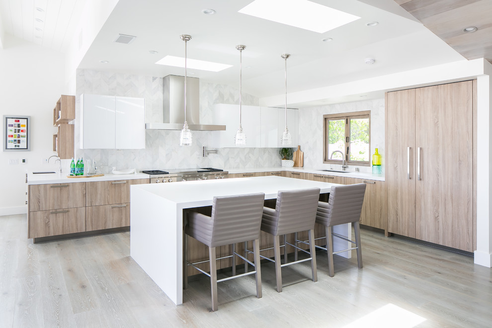 Cette photo montre une cuisine tendance en L et bois clair avec un placard à porte plane, un électroménager en acier inoxydable, parquet clair, îlot, un sol beige et un plan de travail blanc.