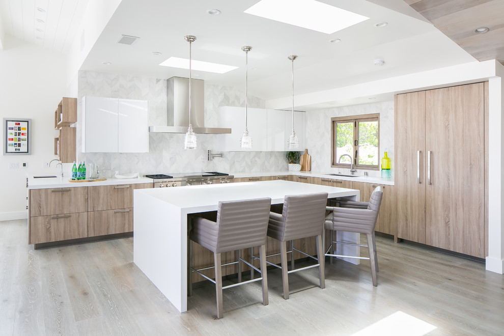 Foto på ett funkis vit l-kök, med en undermonterad diskho, släta luckor, skåp i mellenmörkt trä, vitt stänkskydd, rostfria vitvaror, ljust trägolv, en köksö och grått golv