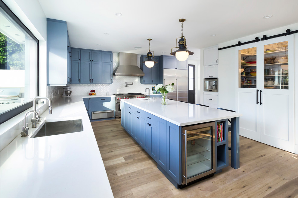 Immagine di una cucina a L tradizionale con lavello sottopiano, ante in stile shaker, ante blu, paraspruzzi bianco, elettrodomestici in acciaio inossidabile e pavimento beige