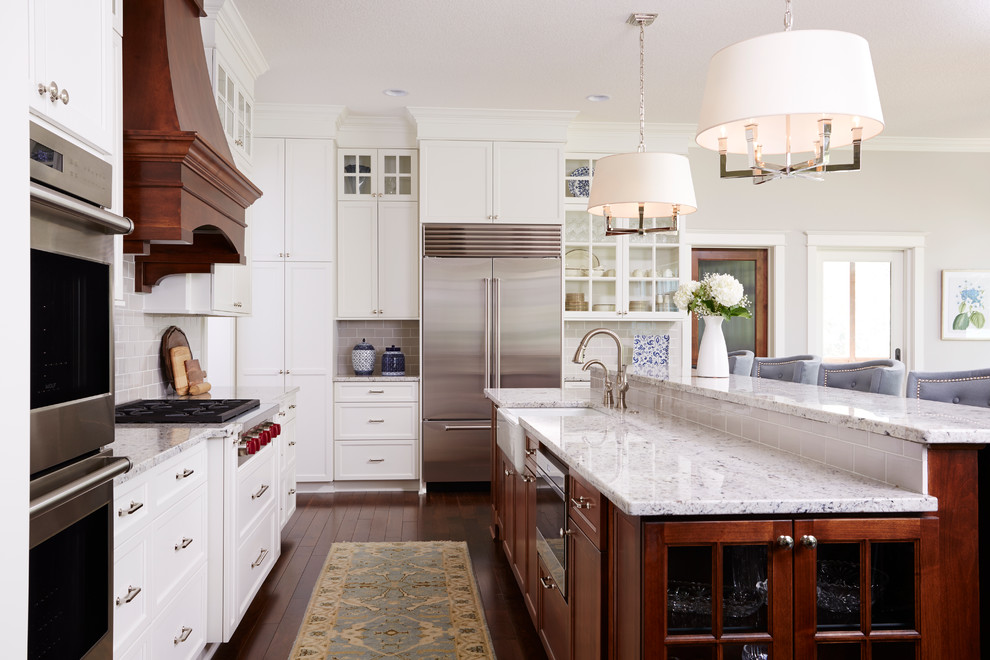 Klassisk inredning av ett kök, med en rustik diskho, luckor med glaspanel, grått stänkskydd, stänkskydd i tunnelbanekakel, rostfria vitvaror, mellanmörkt trägolv och en köksö