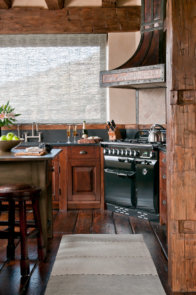 На фото: кухня в стиле рустика с фасадами цвета дерева среднего тона, гранитной столешницей, черной техникой, паркетным полом среднего тона, бежевым фартуком и шторами на окнах с