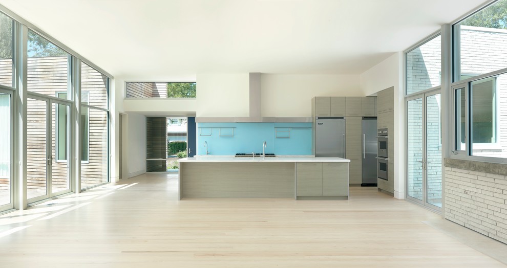Стильный дизайн: параллельная кухня-гостиная в стиле модернизм с плоскими фасадами, светлыми деревянными фасадами, мраморной столешницей, синим фартуком, фартуком из стекла, техникой из нержавеющей стали и островом - последний тренд
