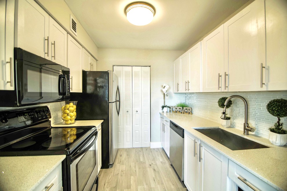 Enclosed kitchen - small transitional galley laminate floor and beige floor enclosed kitchen idea in Miami with an undermount sink, shaker cabinets, white cabinets, laminate countertops, gray backsplash, ceramic backsplash, stainless steel appliances, no island and white countertops