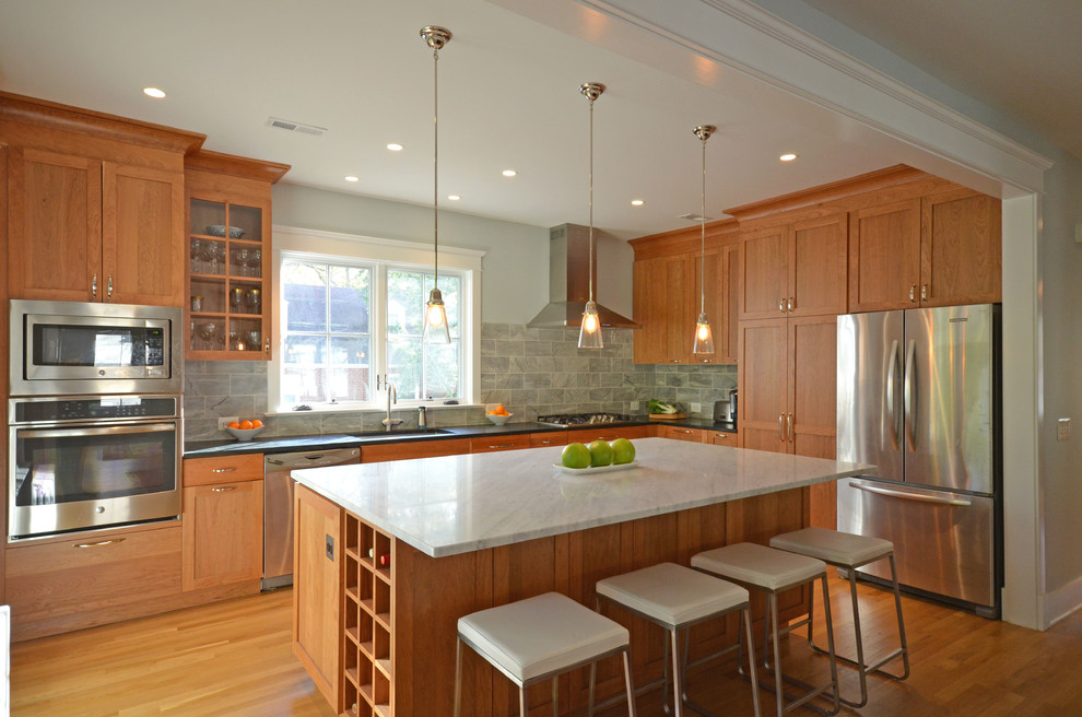 Large transitional l-shaped medium tone wood floor eat-in kitchen photo in DC Metro with an undermount sink, shaker cabinets, medium tone wood cabinets, soapstone countertops, gray backsplash, stone tile backsplash, stainless steel appliances and an island