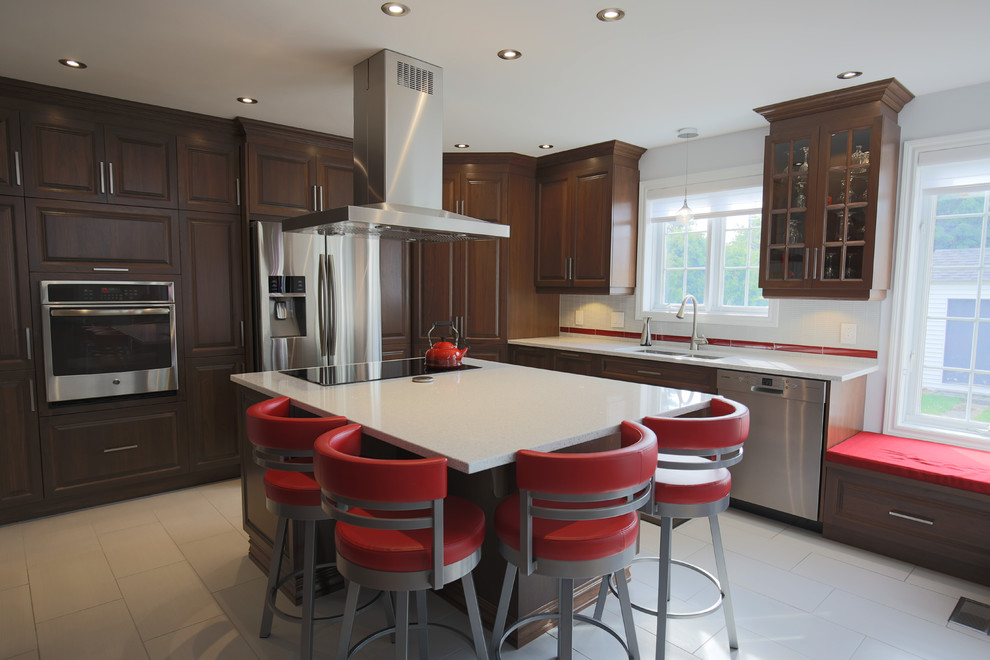 This is an example of a large classic l-shaped kitchen in Montreal with a submerged sink, stainless steel appliances, porcelain flooring, beige floors, raised-panel cabinets, dark wood cabinets, composite countertops, white splashback, glass tiled splashback and an island.
