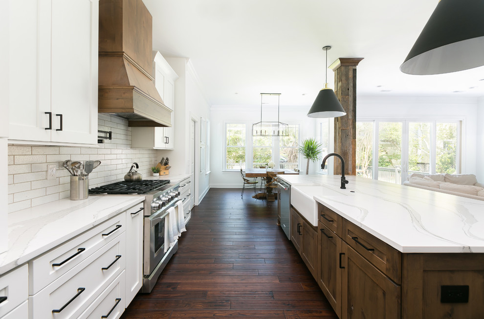 Open concept kitchen - huge cottage galley dark wood floor and brown floor open concept kitchen idea in Charleston with a farmhouse sink, shaker cabinets, white cabinets, quartz countertops, white backsplash, brick backsplash, stainless steel appliances, an island and white countertops