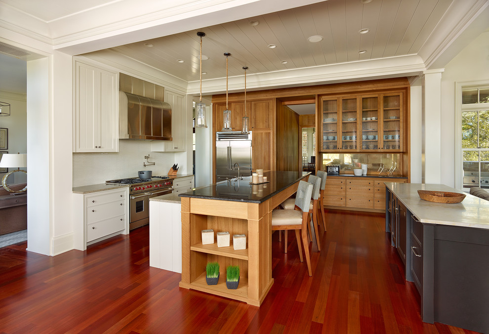 Aménagement d'une cuisine classique en bois brun avec un placard à porte vitrée, un électroménager en acier inoxydable et une crédence blanche.