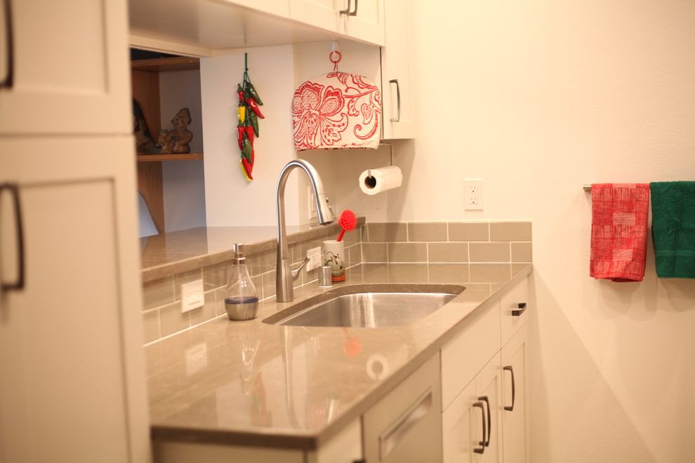 Modelo de cocina comedor escandinava pequeña con fregadero encastrado, puertas de armario blancas, salpicadero de azulejos tipo metro y electrodomésticos de acero inoxidable