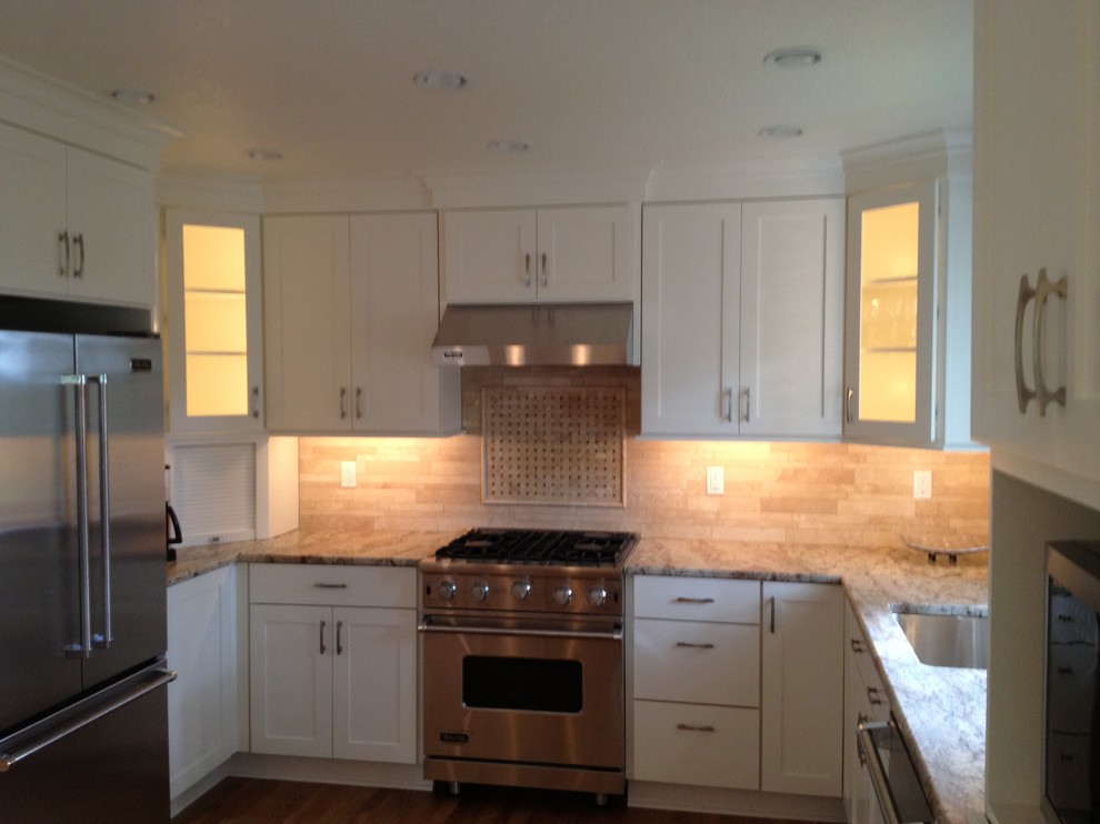 Example of a mid-sized classic u-shaped medium tone wood floor eat-in kitchen design in Portland with an undermount sink, shaker cabinets, white cabinets, granite countertops, stone tile backsplash, stainless steel appliances, an island and beige backsplash