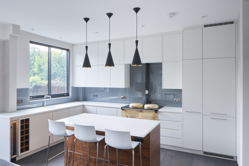 This is an example of a large contemporary open plan kitchen in London with an integrated sink, flat-panel cabinets, white cabinets, grey splashback, glass sheet splashback, dark hardwood flooring and an island.