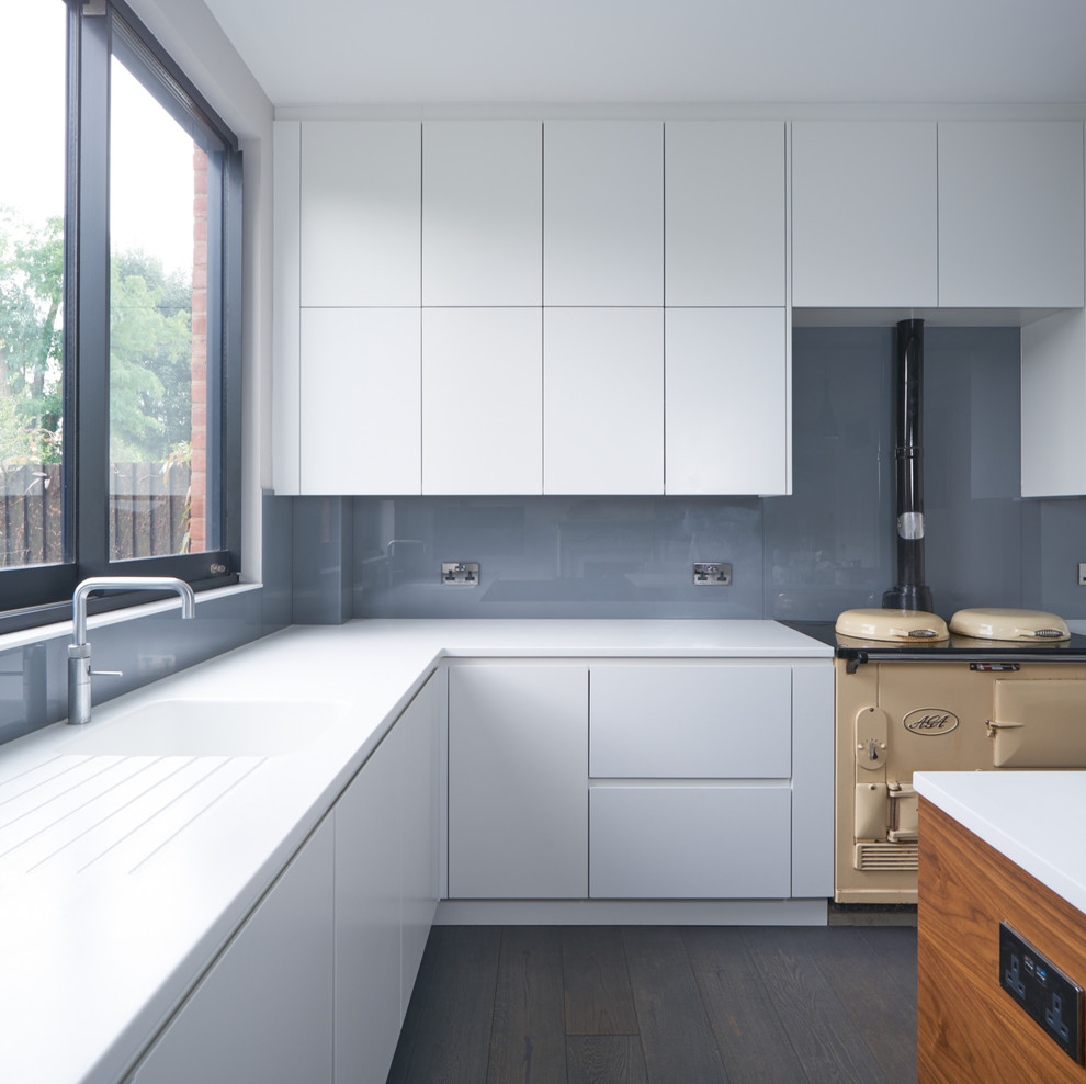 Photo of a large contemporary open plan kitchen in London with an integrated sink, flat-panel cabinets, white cabinets, grey splashback, glass sheet splashback, dark hardwood flooring and an island.
