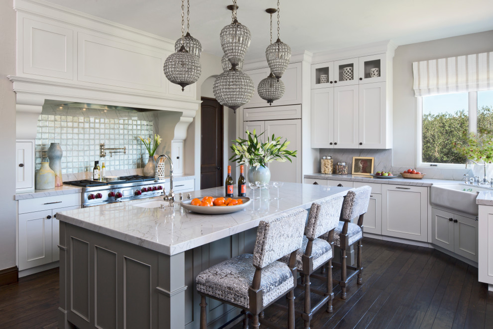 Inspiration for a mediterranean u-shaped dark wood floor and brown floor kitchen remodel in Los Angeles with a farmhouse sink, recessed-panel cabinets, white cabinets, metallic backsplash, stainless steel appliances, an island and white countertops