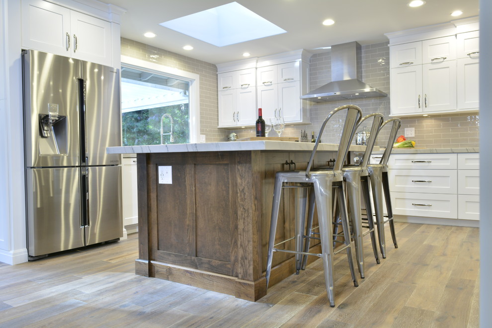 Large transitional l-shaped light wood floor eat-in kitchen photo in San Francisco with a drop-in sink, beaded inset cabinets, white cabinets, quartzite countertops, gray backsplash, subway tile backsplash, stainless steel appliances and an island