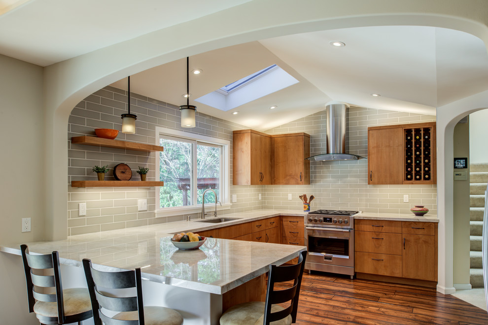 Example of a trendy u-shaped medium tone wood floor and brown floor kitchen design in San Francisco with an undermount sink, flat-panel cabinets, medium tone wood cabinets, gray backsplash, subway tile backsplash, stainless steel appliances, a peninsula and white countertops