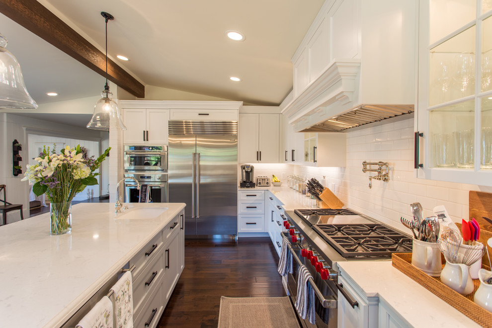 Farmhouse kitchen in San Francisco with a submerged sink, shaker cabinets, white cabinets, engineered stone countertops, white splashback, ceramic splashback, stainless steel appliances, dark hardwood flooring, an island and brown floors.