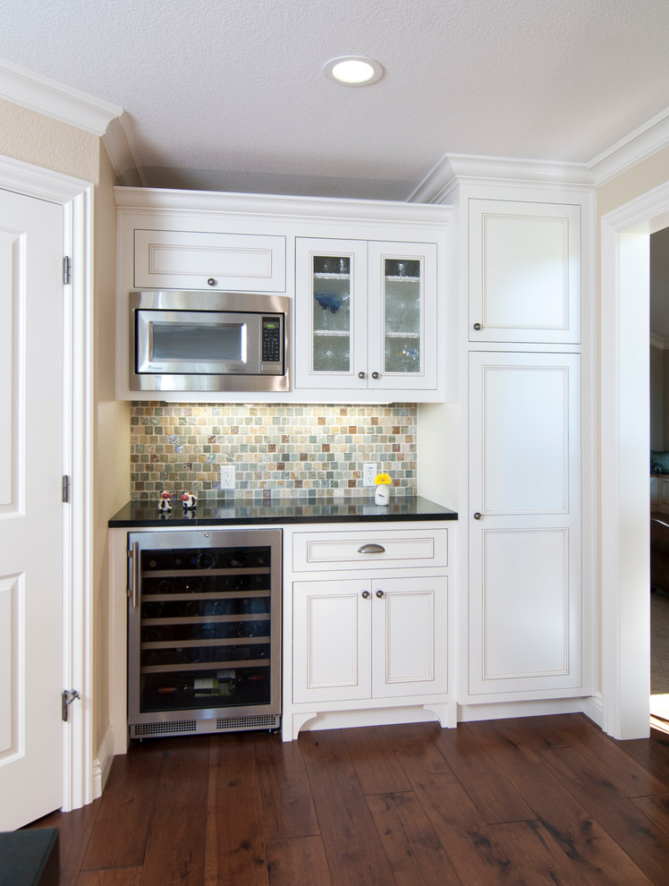 Inspiration for a transitional l-shaped dark wood floor eat-in kitchen remodel in San Francisco with a farmhouse sink, white cabinets, soapstone countertops, beige backsplash, ceramic backsplash, stainless steel appliances, an island and shaker cabinets