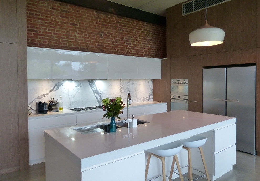Expansive industrial l-shaped open plan kitchen in Adelaide with a submerged sink, flat-panel cabinets, white cabinets, engineered stone countertops, multi-coloured splashback, stainless steel appliances, concrete flooring, an island, marble splashback and grey floors.