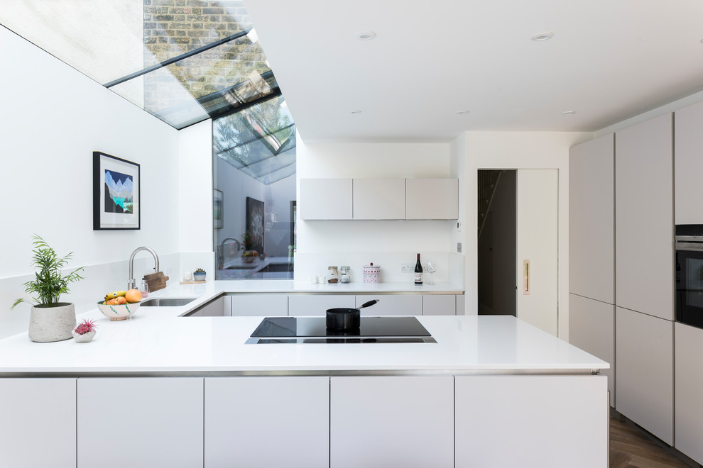 Moderne Küche in U-Form mit Unterbauwaschbecken, flächenbündigen Schrankfronten, grauen Schränken, Halbinsel und weißer Arbeitsplatte in London
