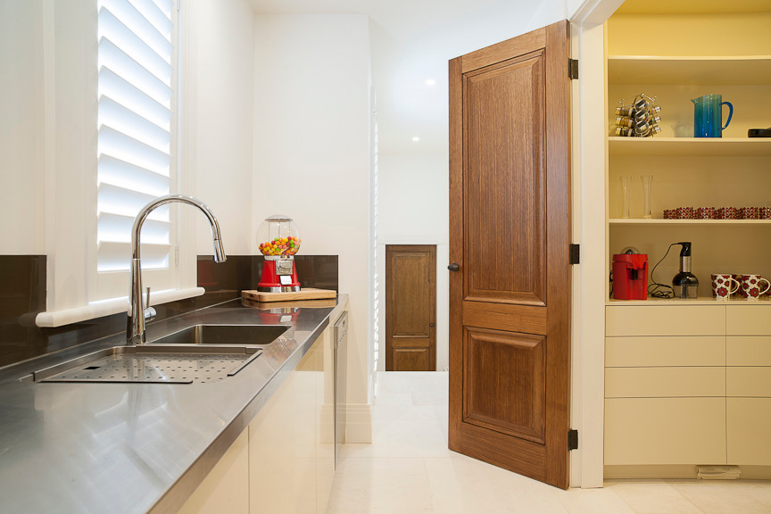 This is an example of an expansive contemporary galley kitchen pantry in Melbourne with an integrated sink, flat-panel cabinets, beige cabinets, stainless steel worktops, brown splashback, stone slab splashback, stainless steel appliances and limestone flooring.