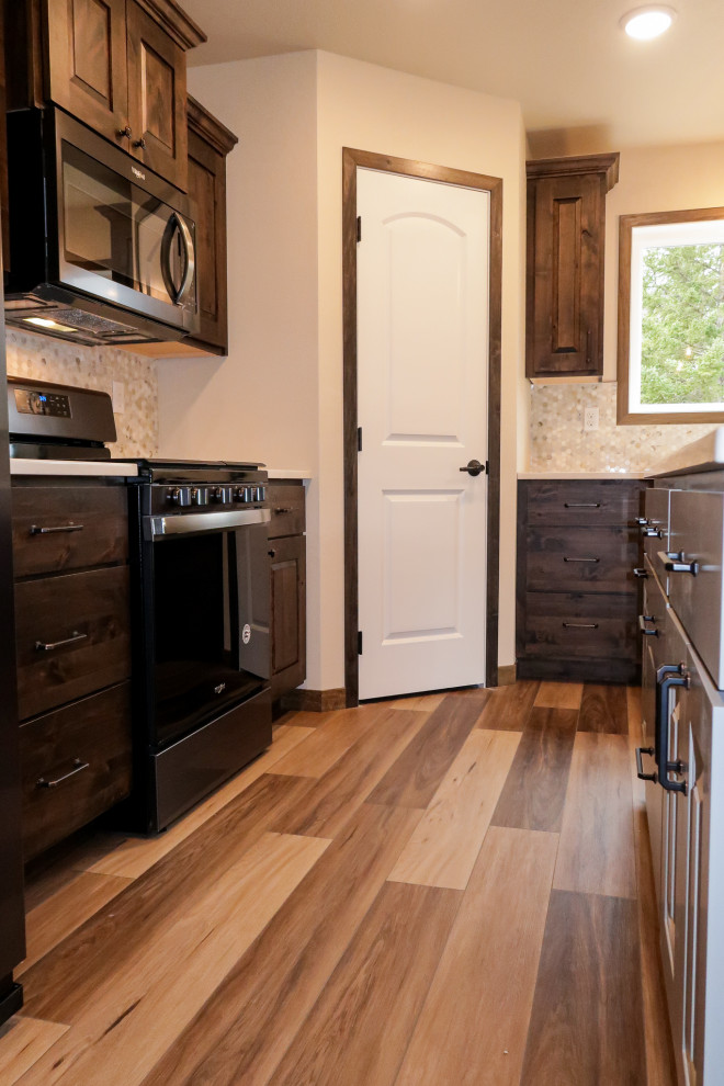 Example of a mid-sized classic l-shaped vinyl floor and brown floor kitchen design in Other with a farmhouse sink, raised-panel cabinets, brown cabinets, quartz countertops, white backsplash, stone tile backsplash, black appliances, an island and white countertops