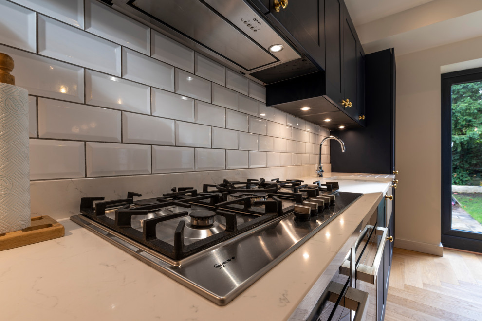 Bild på ett funkis kök och matrum, med skåp i shakerstil, blå skåp, vitt stänkskydd, stänkskydd i keramik, ljust trägolv och en köksö