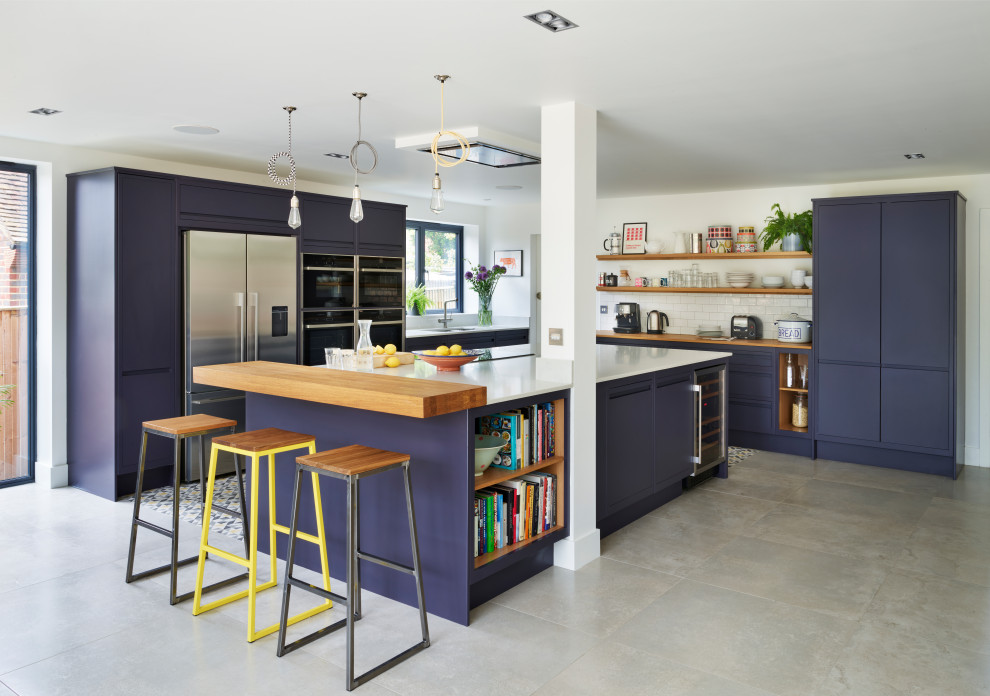 Contemporary l-shaped kitchen in London with a submerged sink, flat-panel cabinets, blue cabinets, wood worktops, white splashback, metro tiled splashback, stainless steel appliances, an island, grey floors and white worktops.