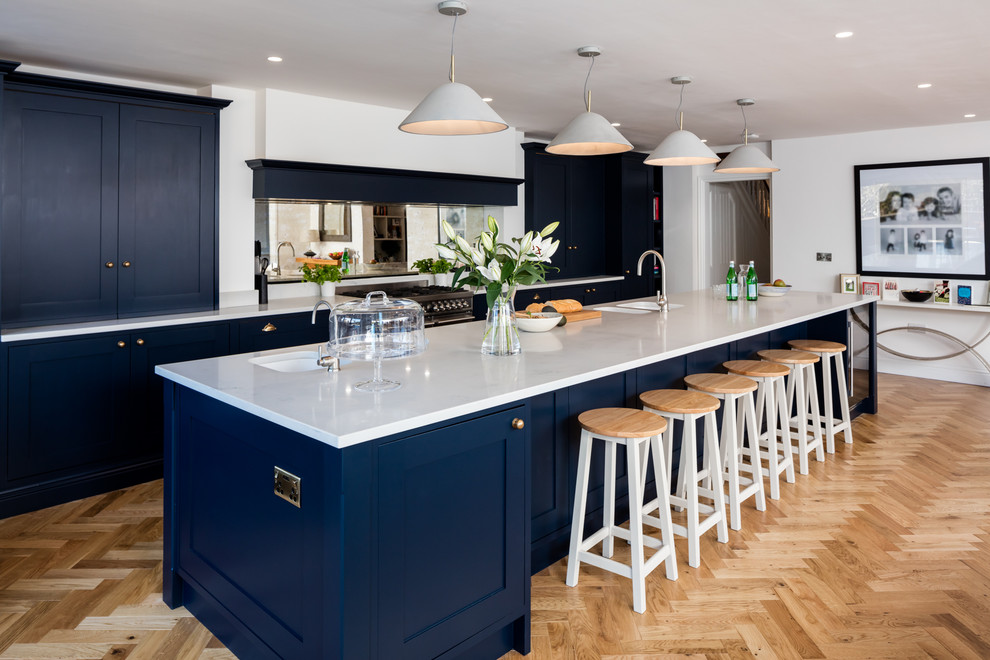 バークシャーにある広いトランジショナルスタイルのおしゃれなキッチン (ダブルシンク、落し込みパネル扉のキャビネット、青いキャビネット、ミラータイルのキッチンパネル、淡色無垢フローリング、ベージュの床) の写真